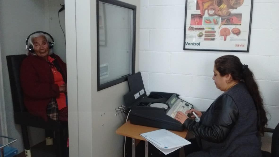Adulta mayor con audífonos durante una audiometría en cabina insonorizada
